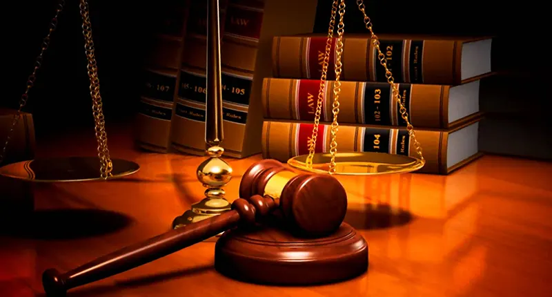 A wooden gavel and scales of justice placed on a table near law books.