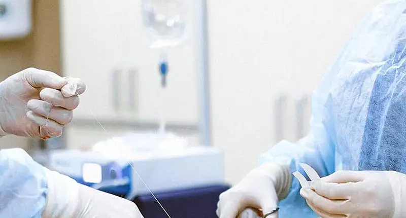 Medical professionals in surgical attire handling instruments during a procedure.