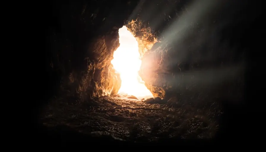 Bright light streaming from an opening in a dark cave, illuminating the rocky interior.