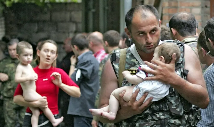 A man in military attire holding a baby while another child is being carried by a woman nearby.