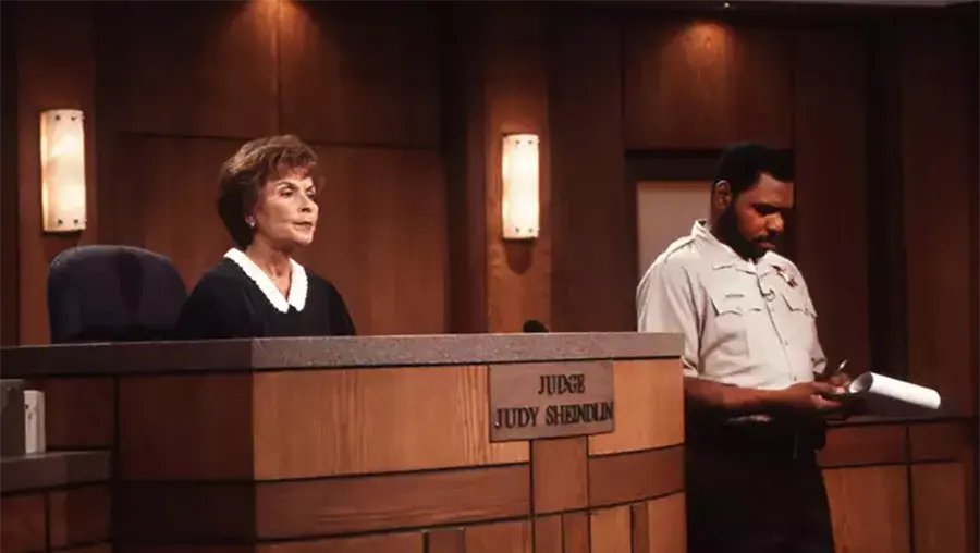 Judge Judy Sheindlin presiding over a courtroom with a bailiff standing nearby.