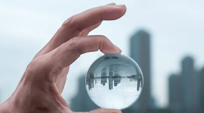 A hand holding a clear glass sphere that reflects a city skyline in its surface.