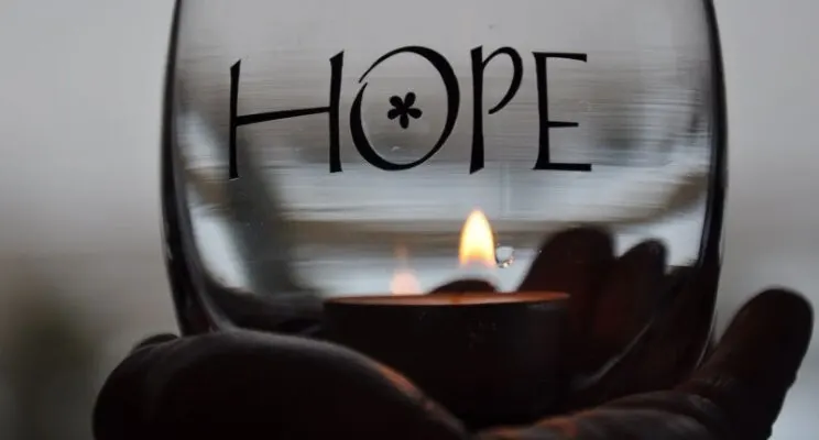 A glass container with the word 'HOPE' inscribed and a lit candle inside.