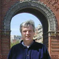 A man with gray hair standing under a stone archway in an outdoor setting.