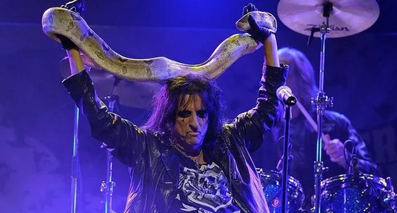 Alice Cooper holding a large snake above his head during a live performance on stage.