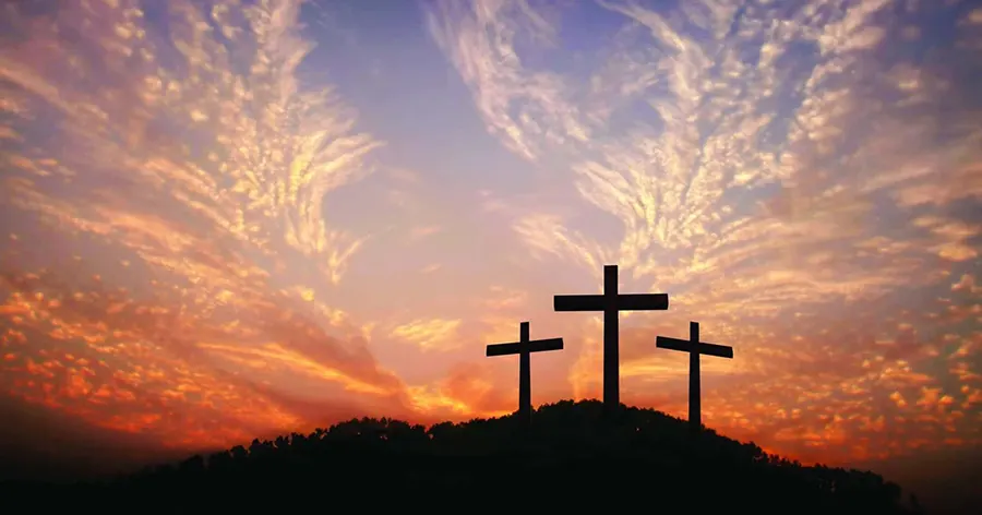 Silhouette of three crosses on a hill during a colorful sunset with clouds.