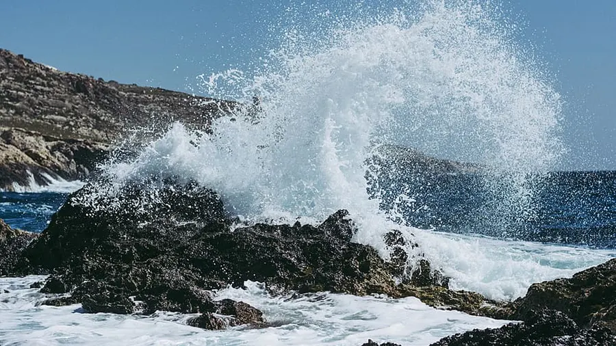 Waves crashing against dark rocks along a coastline with splashes of water.