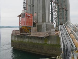 Elevator structure on a pier with concrete columns and scaffolding, showcasing industrial design and functionality in a marine environment.