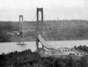 Black and white image of a suspension bridge spanning a river with towers and cables.