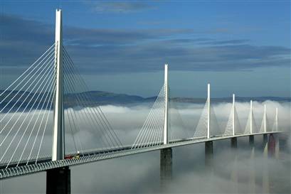 Millau Viaduct, a cable-stayed bridge, spans through fog with multiple towers and cables visible.