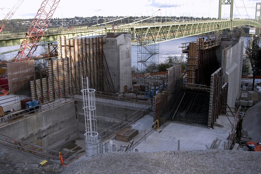 Construction site showing concrete forms and scaffolding for bridge support structures.