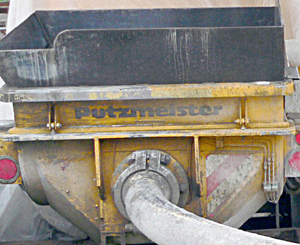 Putzmeister concrete pump equipment with a yellow and black design, showcasing the machine's hopper and discharge hose.