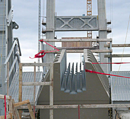 Construction site featuring a large concrete beam being installed with scaffolding and safety measures in place.