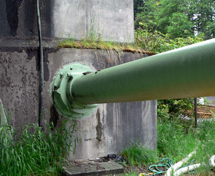 A large green industrial pipe connected to a concrete wall, showcasing industrial infrastructure and engineering.