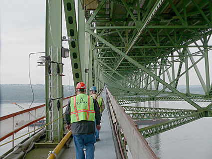 Two workers in safety vests inspecting the green structure of a bridge, showcasing engineering and maintenance activities.