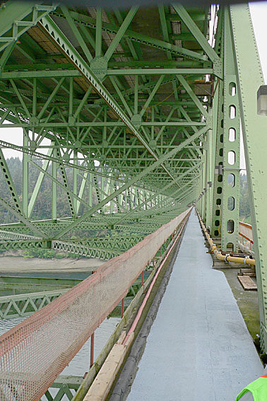 A view of a green steel bridge showcasing its intricate framework and supporting beams, emphasizing engineering design and construction.