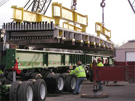 Heavy Equipment Loading Process Heavy machinery being loaded onto a flatbed truck with cranes and workers overseeing the operation.