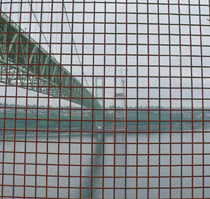 A view of a green bridge through a grid pattern, showcasing the structure and surrounding water.