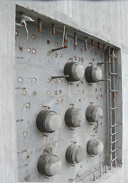 Concrete wall featuring embedded circular fixtures and exposed rebar, showcasing industrial construction elements and structural components.