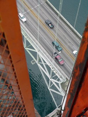 Aerial view of vehicles on a bridge above a waterway, showcasing the structure and traffic flow, with a focus on the bridge's support beams.