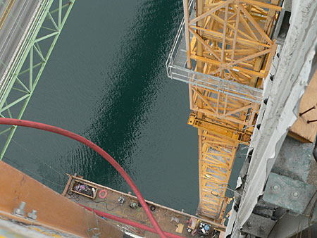 Aerial perspective of a construction site with a crane and water below, showcasing industrial equipment and structures.