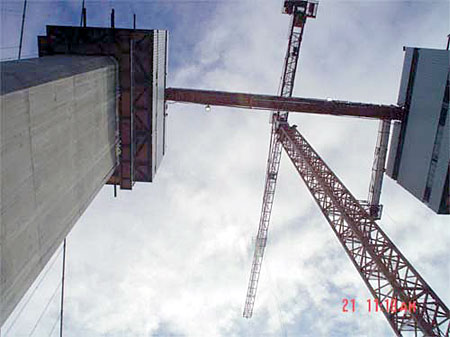 Construction cranes and concrete structure under a cloudy sky, showcasing heavy machinery and building progress.