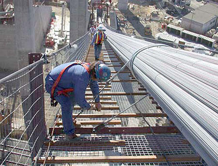 Construction Workers on Bridge Project Construction workers installing cables on a bridge, showcasing safety gear and structural elements, emphasizing engineering and construction.