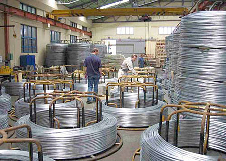 Coiled Steel Wire in Warehouse Coiled steel wire rolls in a warehouse with workers inspecting the material, showcasing industrial storage and manufacturing processes.