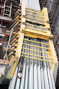 Lifting equipment for steel beams with a yellow frame and multiple steel rods stacked vertically.