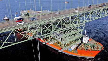 Cargo Ship Under Bridge A cargo ship navigating under a bridge with vehicles on top, showcasing maritime transport and infrastructure.
