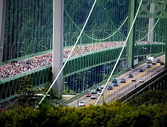 Crowd on the Green Bridge A large crowd walking on a green bridge with vehicles on the lower roadway.