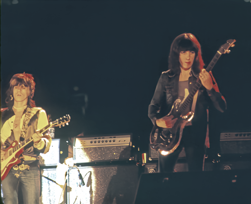 Rolling Stones performing on stage with guitars and amplifiers in the background, showcasing a live music event atmosphere.