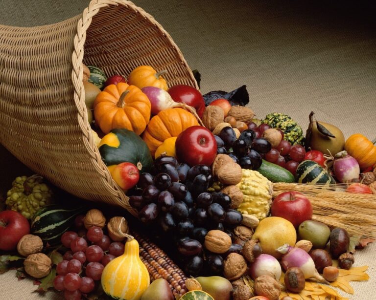 A cornucopia overflowing with assorted fruits, vegetables, and nuts on a neutral background.