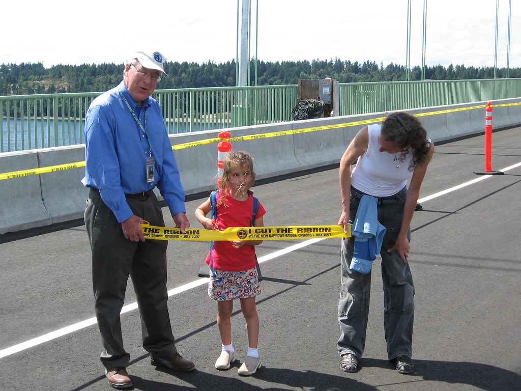 Ribbon Cutting Ceremony with Child and Adults A man and a child holding a ribbon labeled 'Cut the Ribbon' with a woman standing beside them at a ceremony.
