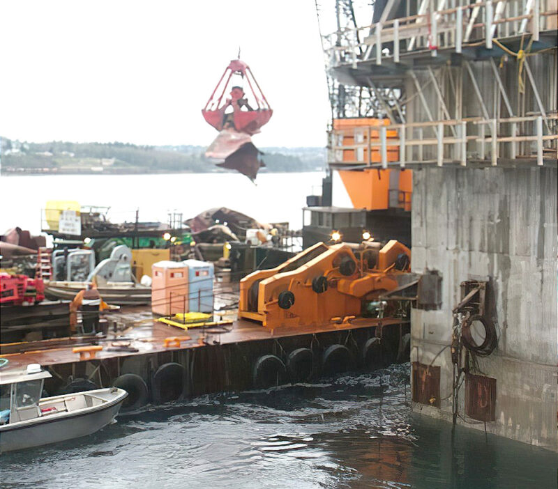 Heavy industrial equipment and machinery on a dock with a crane and cargo containers.