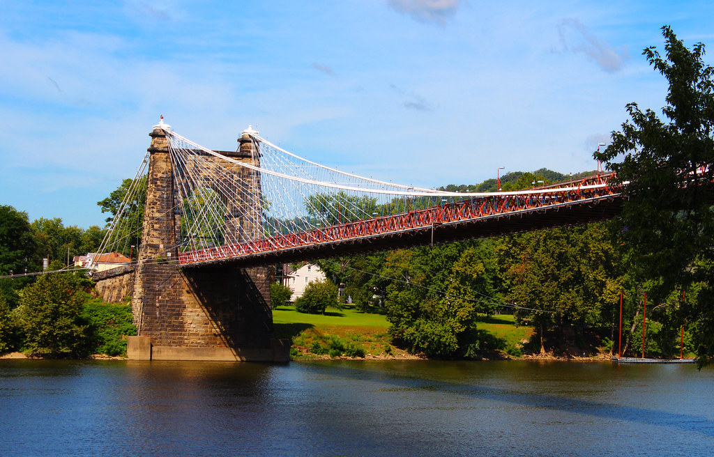 Wheeling Suspension Bridge spanning the Ohio River, showcasing its stone towers and suspension cables against a clear blue sky.