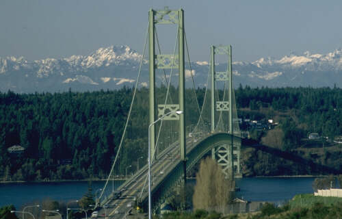 Second Tacoma Narrows Bridge spanning over water with snow-capped mountains in the background, showcasing a scenic view of nature and infrastructure.