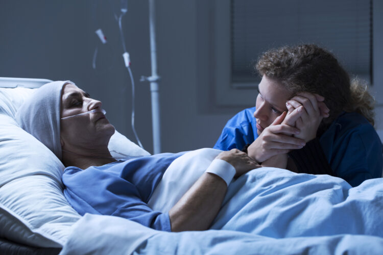 A caregiver comforting a patient in a hospital bed, illustrating end-of-life care and emotional support in a healthcare setting.